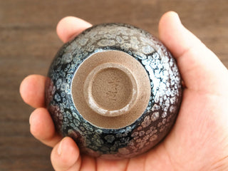 Base of a Shu Kou sky eye oil spot Jianzhan bowl held in hand, showing the unglazed foot ring and an impressed jian (建) makers mark.
