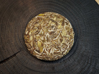 Close-up of the unwrapped Silk Ray white tea cake showing high-quality silver buds and dark green compressed leaves on a dark wooden background.
