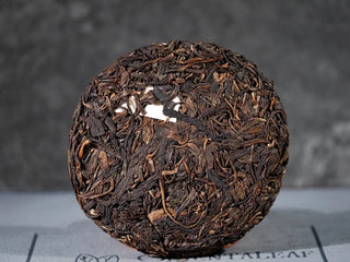 Front view of unwrapped Yiwu Raw Pu-erh Cake – 2013 Spring Tea, Hand-Pressed 2023, Sweet & Layered (100g), highlighting the dark glossy tea leaves and round cake shape