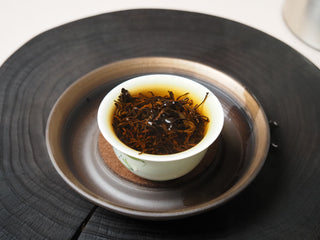 Yunnan Shaken-Leaf Black Tea steeping inside a white porcelain gaiwan during the brewing process.