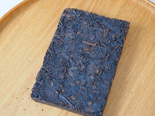 Close-up texture view of the 2013 Dry-Aged Lincang Ripe Pu-erh Ancient Tree Tea Brick placed on a round wooden tray.