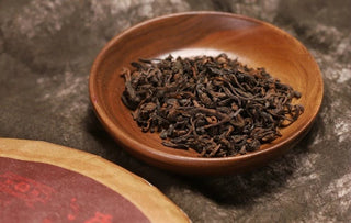 Dry 2017 Bojun Ripe Pu-erh leaves in a light wooden bowl, dark fermented leaves with golden buds, on a beige linen cloth.