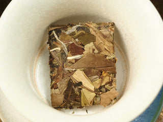 2018 indoor-withered Fuding White Peony compressed tea biscuit placed in a white ceramic gaiwan, top view before brewing.