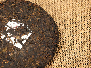Angled view of Jing Chang Hao Quiet Years 2018 raw Pu-erh cake edge showing loosely compressed arbor leaves and the nei fei label corner