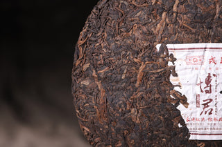 Close detail of the 2019 Bojun 500g cake, showing the inner ticket with calligraphy and pressed dark leaves with golden buds.