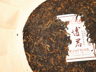 Close detail of the left half of the 2020 Bojun 500g cake, inner ticket and pressed dark leaves with golden tips.