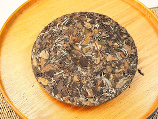 Overhead view of the whole 2020 Fuding Sun-Dried White Peony 350g cake on a wooden serving tray, leaves and buds clearly visible.