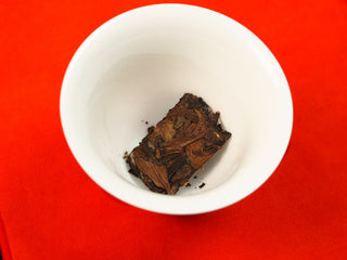 Break-apart section of 2024 Shou Mei and Chen Pi waffle cake placed in a white ceramic gaiwan on a red cloth before brewing.