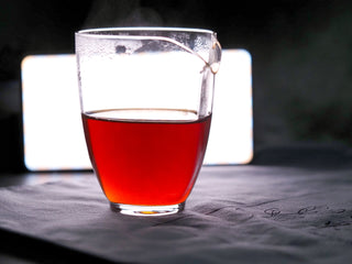 Clear and bright reddish-brown liquor of 2006 aged Liubao tea in a glass cup against light.