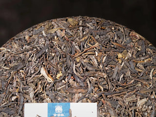 Close-up view of the front surface of Ancient Arbor Harmony Raw Pu-erh Tea cake, highlighting the dry leaf texture and color.