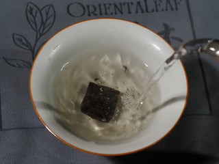 Yunnan Mini Raw Pu-erh Tea Brick being brewed in a gaiwan with hot water, showing infusion process