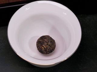 Single Yiwu Raw Pu-erh Dragon Pearl placed in a white porcelain Gaiwan for steeping.