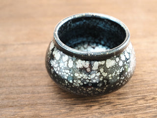 Front low-angle view of a Fo Du Jianzhan tea bowl with large silver oil-spot crystals and faint blue-green iridescence on the dark exterior glaze.