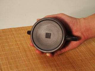 Underside of the Heini Dezhong Yixing teapot held in hand, showing the square maker's seal stamp at the center
