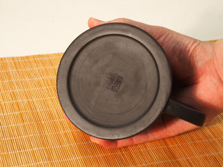 Hand holding a Black Zhu Ni Shede Yixing teapot upside down, showing the round base with square maker seal stamp