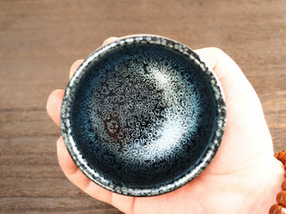 Top view held in hand of a Jiang Jun Bei Jianzhan tea bowl, showing the interior covered with silver oil-spot crystals like a starry sky.
