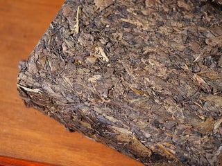 Close-up of a corner of Jingyang Golden Flower Fu Brick Tea showing the layered hand-pressed tea leaves and rich texture of the dark tea brick.