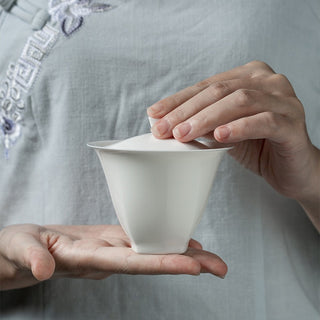 Traditional tea master pouring infusion from a white porcelain gaiwan into a cup