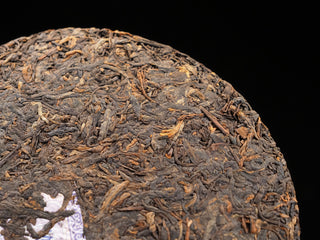 Detailed macro shot of the dry leaf surface of a 2017 Dayi 7452 ripe puerh tea cake, highlighting tight cords and golden tips.