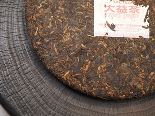 Detailed texture of fermented tea leaves and golden buds on the surface of 2019 Dayi 7572 ripe puerh tea cake.