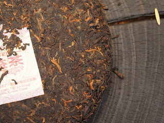 Detailed macro shot of 2019 Dayi 7592 ripe puerh tea cake leaves, showing a blend of dark fermented leaves and coarse tea stems.