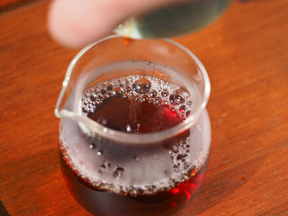Pouring deep amber Da Hong Pao liquor into a glass fairness pitcher (Gongdao Bei).