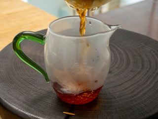 Pouring clear reddish-brown ripe pu-erh tea liquor from a glass fair cup (Gongdao Bei).
