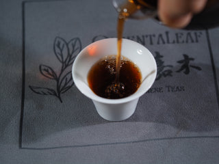 Pouring deep amber Imperial Grade Ripe Puerh tea into a white porcelain cup for a tasting session.

