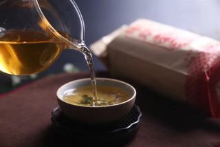 Pouring fresh Yunnan Sheng Puerh tea into a ceramic cup, showcasing the clear amber color.