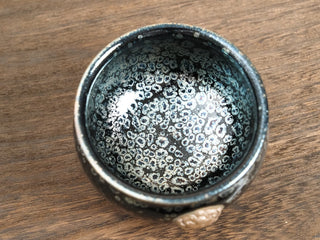 Top-down tilted view of a Rui Shou sky eye oil spot Jianzhan bowl on a wooden table, showing dense ring-shaped silver crystals across the interior and the rim.