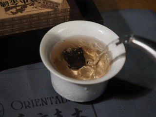A 4g Yunnan Mini Ripe Pu-erh Tea Brick placed in a gaiwan with hot water being poured, showing its easy single-cup brewing method.