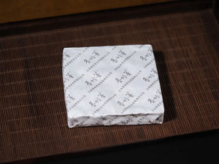 80g Yunnan Raw Pu-erh Waffle Cake mini box unwrapped, showing inner paper packaging on bamboo tea tray
