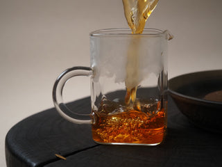 Brewing and pouring clear golden-amber liquor of Yunnan Shaken-Leaf Black Tea into a glass pitcher.