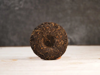 Snow Mountain Rare Wild Ancient Tree Sheng Pu-erh (2016–2023) – 100g Mini Cake, back view unwrapped, showing the uniform tea leaves and compact structure