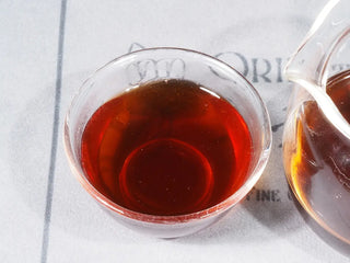 Close-up of the bright, red-hued tea liquor of 2014 Liubao Dark Tea (Betel Nut Aroma & Cooling Finish) in a glass cup.