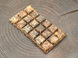 Top view of 2014 sun-dried Fuding Shou Mei 100g waffle cake scored into 18 sections, broad dark leaves with stems pressed firmly.