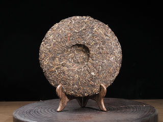 Back view of the unwrapped 2016 Dayi 7532 raw Puerh cake on a stand, showing the traditional central compression dimple.