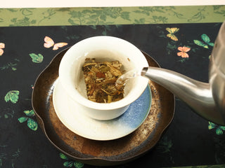 Hot water poured into a white ceramic gaiwan over a 2018 indoor-withered White Peony tea biscuit, beginning to infuse.