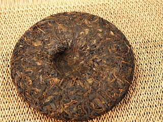 Back of Jing Chang Hao Quiet Years 2018 raw Pu-erh cake showing the center dimple and well-built compressed leaves on a woven mat