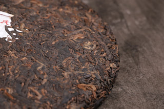 Bottom edge detail of the 2019 Bojun 500g cake, showing tightly pressed dark fermented leaves with golden tips.
