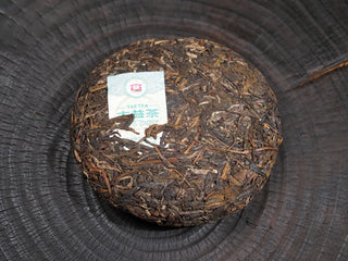 The compressed leaves on the front surface of the 2020 Dayi 7542 raw puerh tea cake with its inner ticket.