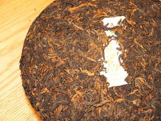 Close detail of the Bojun Ripe Pu-erh 7.0 cake surface, showing tightly pressed dark fermented leaves with golden buds.