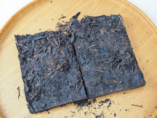 Broken pieces and loose leaves of the 2013 Dry-Aged Lincang Ripe Pu-erh Ancient Tree Tea Brick on a wooden tray.