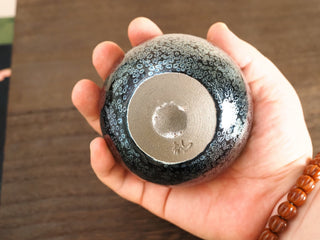 Base of a Bu Dao Weng sky eye oil spot Jianzhan bowl held in hand, showing the unglazed foot ring and a small impressed makers mark.