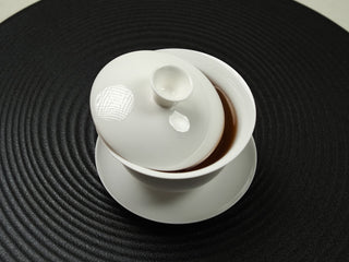 Top-down view of pure white egg-shell porcelain gaiwan with lid ajar revealing amber tea liquor inside