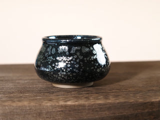 Side profile of a handcrafted Fo Du Jianzhan tea bowl in dark glaze with silver oil-spot pattern, showing the rounded Buddha's belly silhouette.