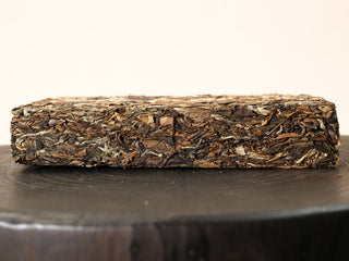 Side view of Gold Brick 2012 sun-dried Fuding White Peony 500g brick showing dense layers of pressed tea leaves and stems.