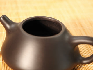 Top-down close-up of a Black Zhu Ni Ziye Shipiao Yixing teapot opening, lid removed, with interior seal visible on bamboo mat