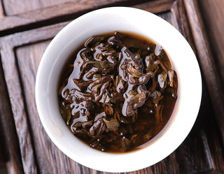 Wet tea leaves of 2019 ancient tree ripe Pu-erh in a white porcelain bowl, showing supple and fat leaf bottom.