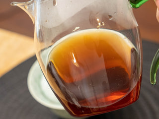 Close-up of the bright amber-red tea liquor of brewed Mang Fei 2022 shou puerh in a glass pitcher.